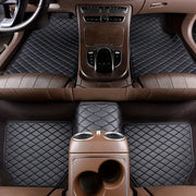 Car interior with black quilted floor mats and brown leather seats.